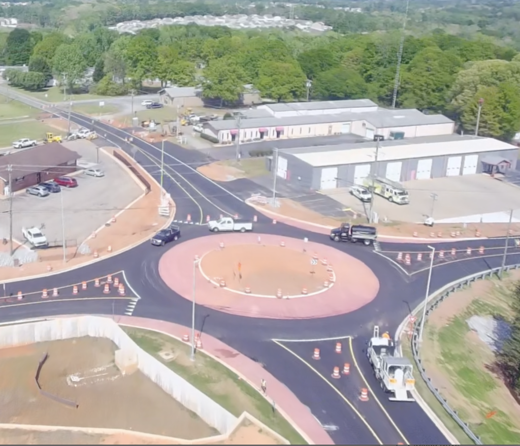 A freshly paved roundabout located amid industrial buildings and new construction lots.
